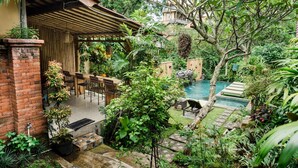 A lush garden with a pool, a wooden deck, and a brick wall. - Desak Putu Putra Hidden (Ubud)