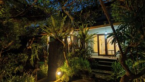 A house surrounded by dense vegetation at night with a well-lit entrance. - Desak Putu Putra Hidden (Ubud)