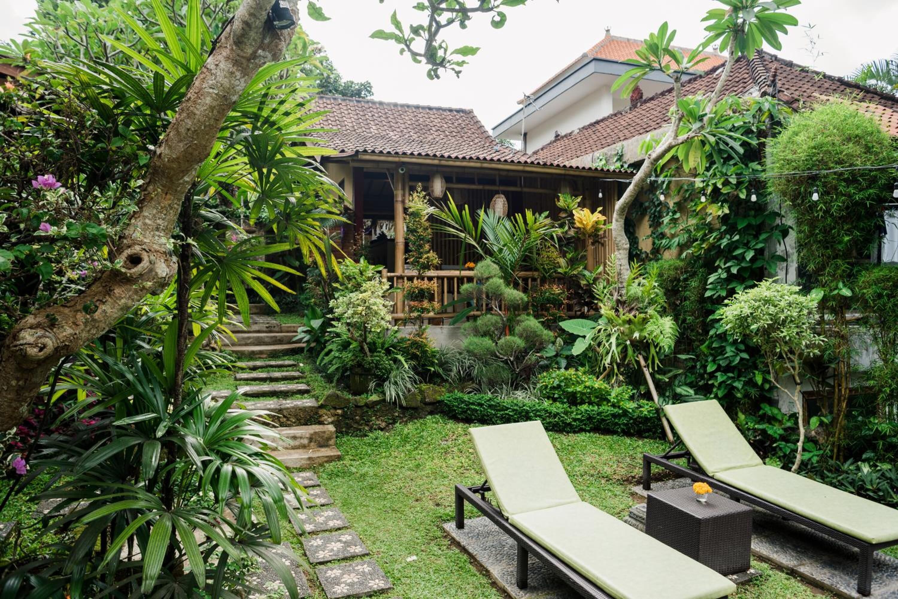 Um jardim com duas espreguiçadeiras, um deck de madeira e diversas plantas tropicais.