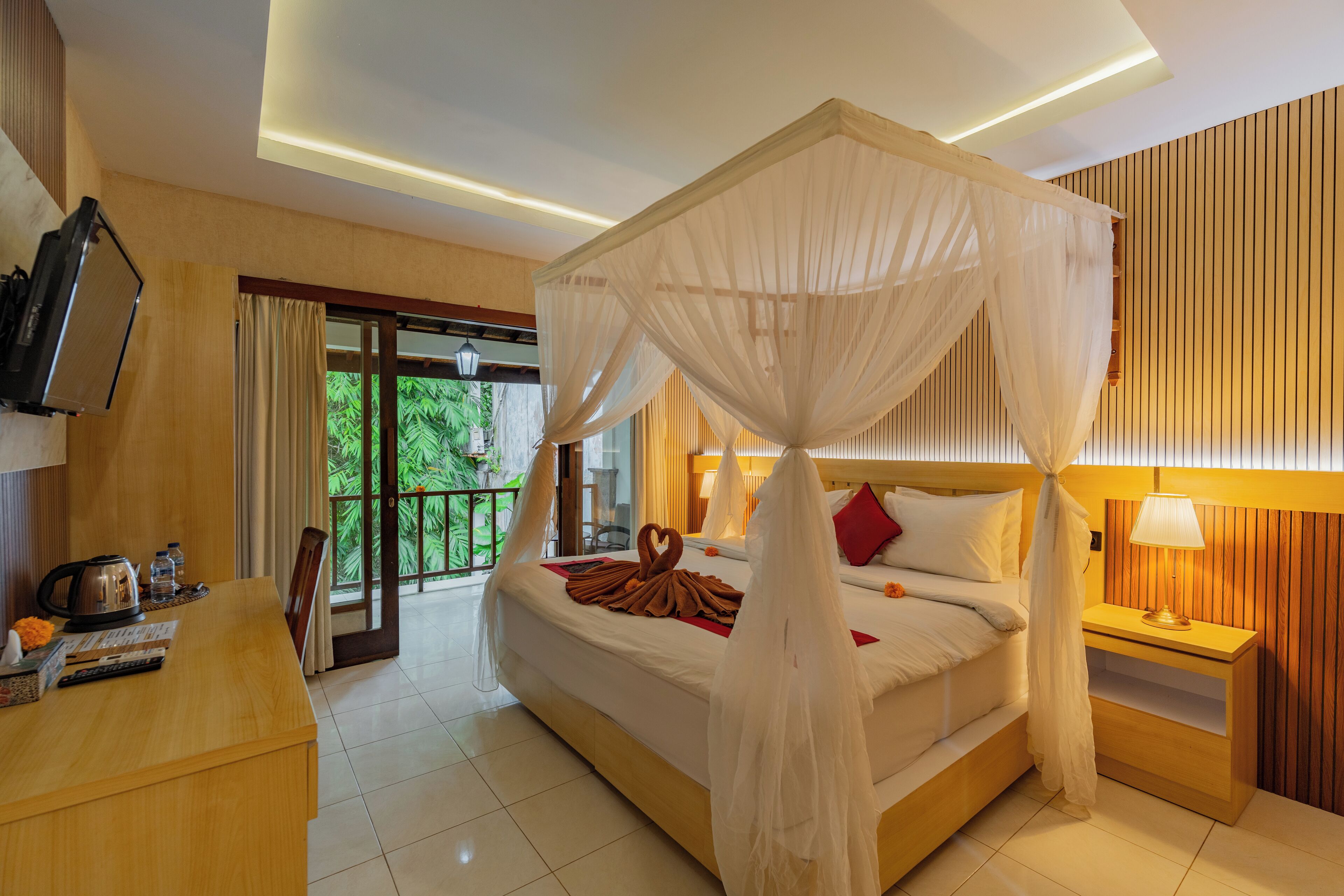A hotel room with a bed, a bedside table, a TV, and a balcony with a view of greenery.
