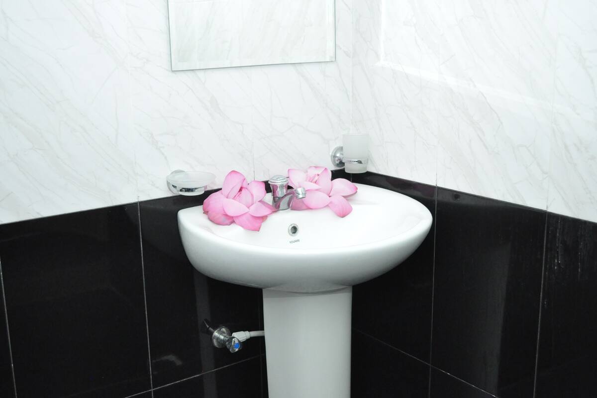 A bathroom with a white pedestal sink, black tiles, and a framed picture on the wall.