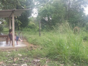 A rustic outdoor seating area with a wooden table and chairs, surrounded by lush greenery and a fence. - Greenwood Udawalawa Safari Resort (Udawalawa)