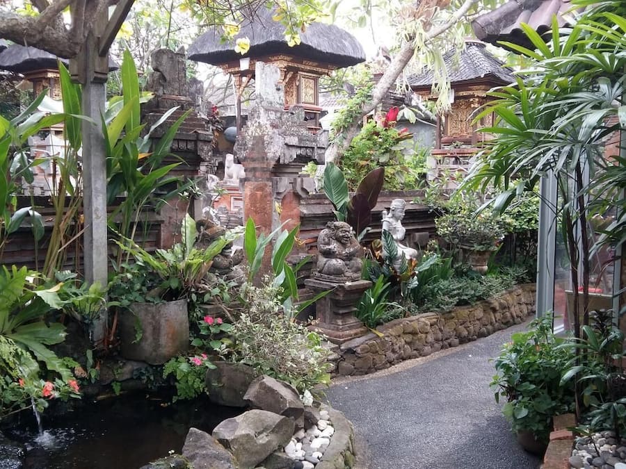 Un complejo de templos balineses tradicional, con estructuras de piedra, un camino de piedra y exuberante vegetación tropical.