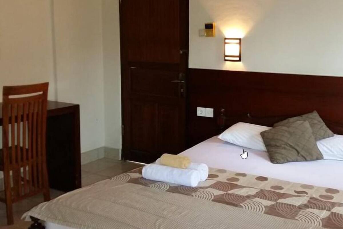 A hotel room with a bed, a chair, a desk, and a door.