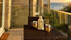 Ein Balkon mit einem Korbstuhl-Tisch, zwei Tassen und einer Laterne.