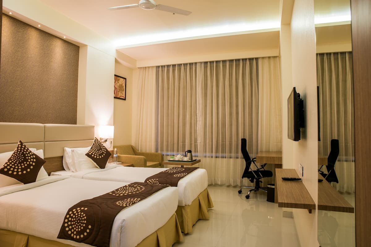 A hotel room with two beds, a desk, a chair, a television, and a ceiling fan.
