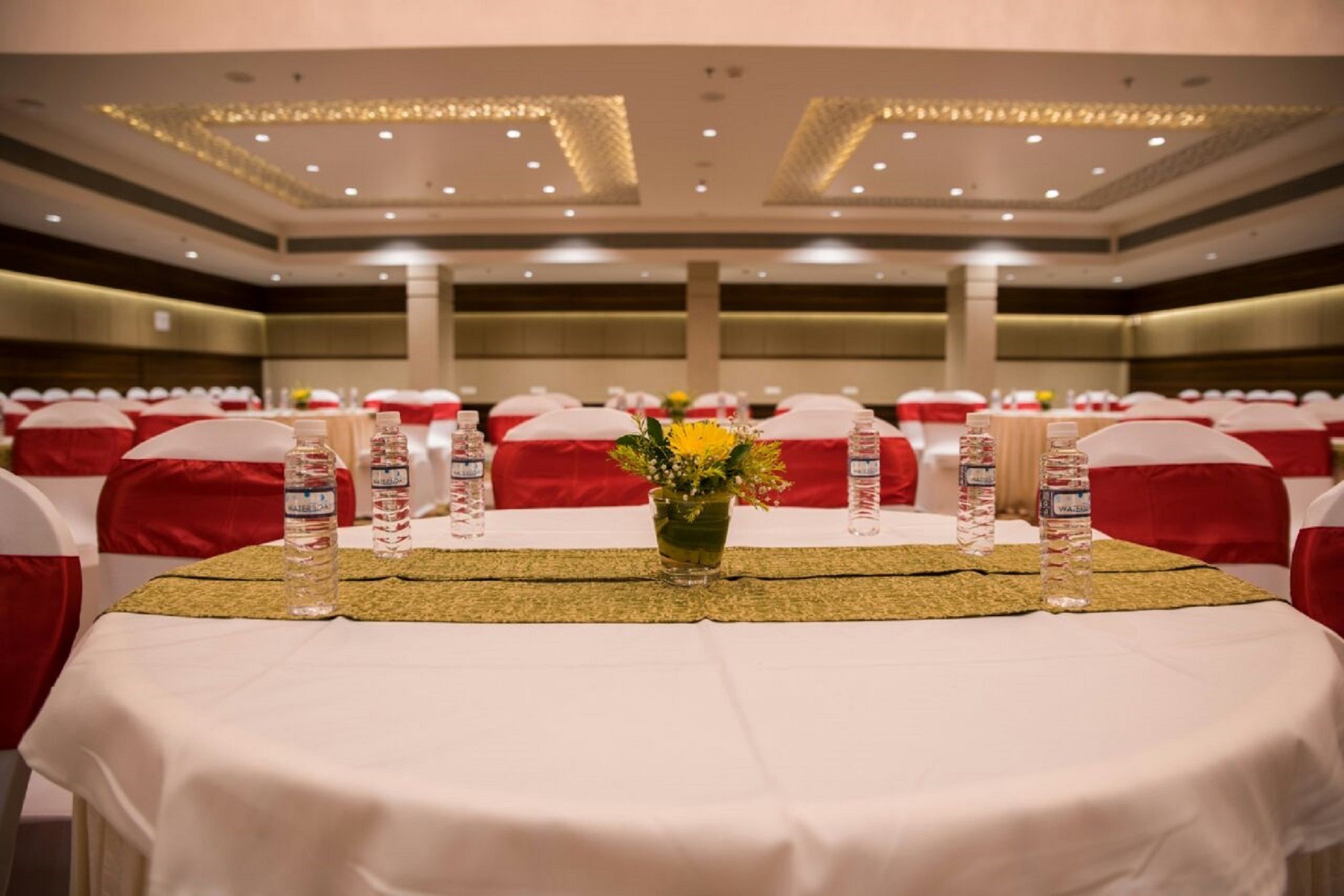 A banquet hall with tables set for a formal event, featuring white tablecloths, red chairs, and water bottles.
