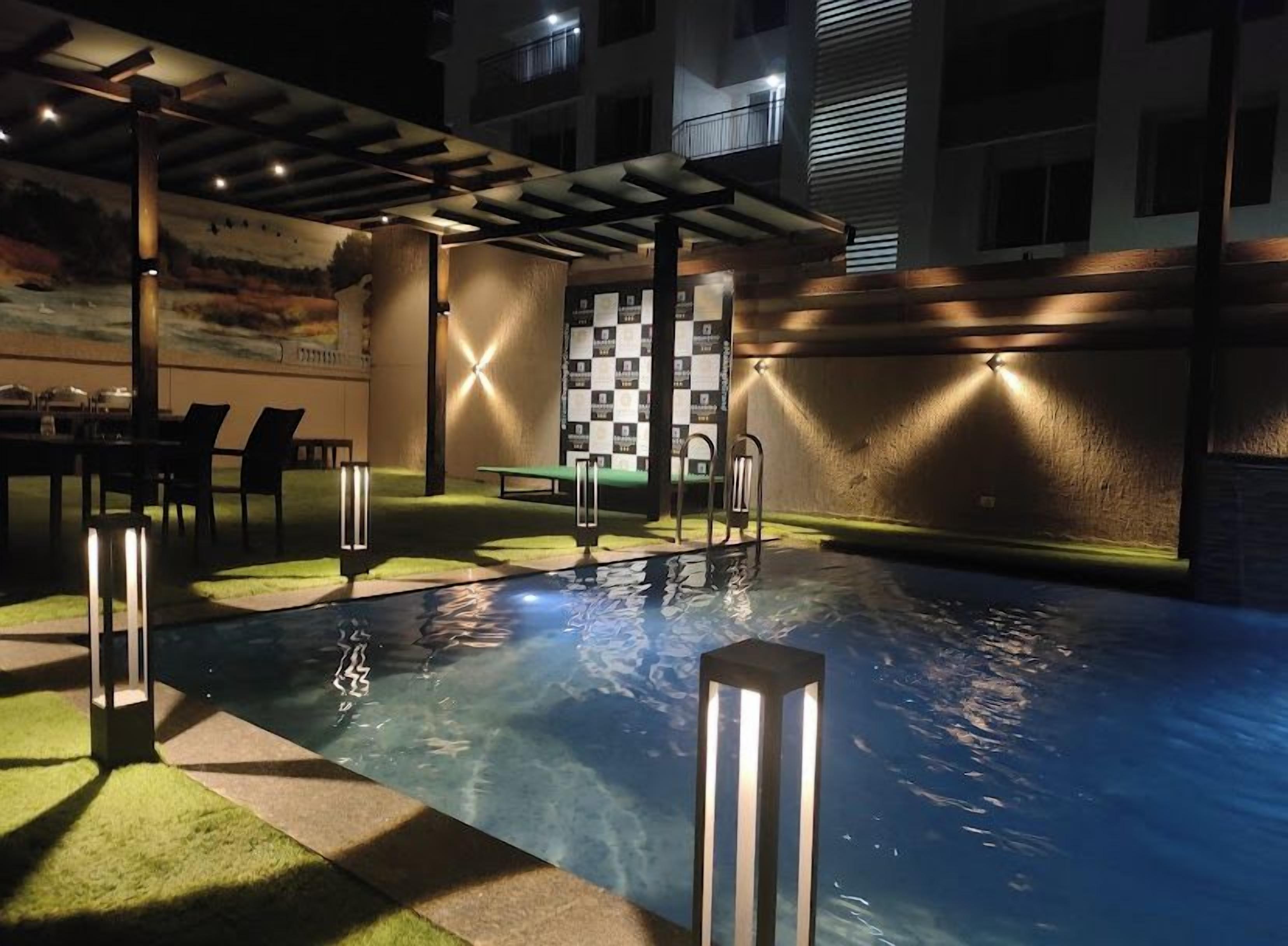 An outdoor swimming pool area with a checkered wall, seating, and lighting fixtures.