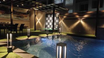 An outdoor swimming pool area with a checkered wall, seating, and lighting fixtures.
