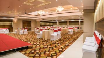 Un amplio salón de banquetes con mesas redondas, sillas blancas y cintas rojas.