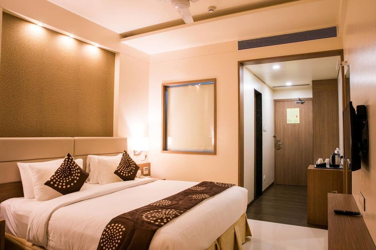 A hotel room with a bed, bedside table, lamp, mirror, and a door leading to a bathroom.