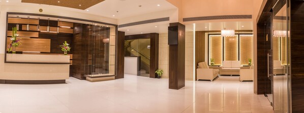 A modern hotel lobby with a reception desk, seating area, and a staircase. - Grand Rio (Nashik)