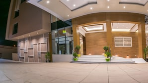A modern building with a curved facade, large windows, and a well-lit entrance area with steps and potted plants.