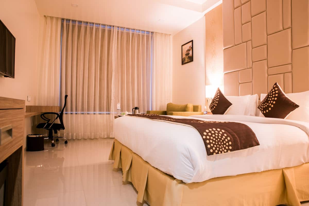 A hotel room with a large bed, a desk, a chair, and a window with curtains.