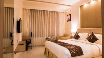 A hotel room with a bed, a desk, a chair, a television, and a window with curtains.