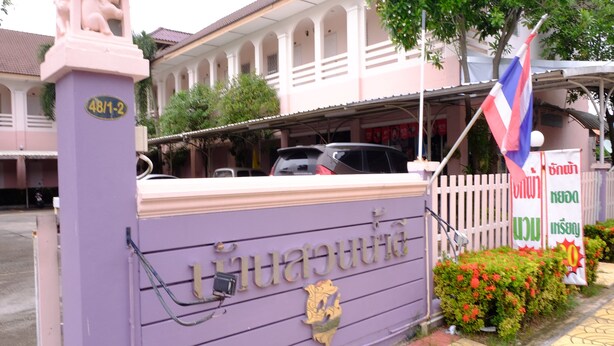 A building with a purple facade, a sign with Thai script, and a flag. - Bansuannamdee (Pluak Daeng)