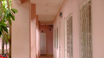 A corridor with a tiled floor, a white door at the end, and a window with metal bars on the right wall.