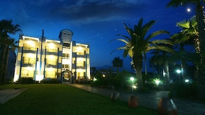 A multi-story hotel with a central tower, surrounded by palm trees and a well-lit entrance. - Hodo House (Seogwipo)