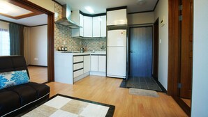 A compact living space with a kitchenette, a sofa with patterned cushions, and a wooden floor. - Hodo House (Seogwipo)