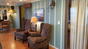 A cozy living room with two patterned armchairs, a wooden coffee table, a lamp, and a painting on the wall.