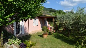 Une villa rose avec un jardin, un chemin de pierre et une colline en arrière-plan.