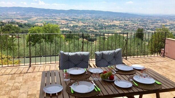 Une table en bois, dressée pour le repas, offre une vue panoramique sur une vallée et des montagnes en arrière-plan.