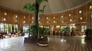 A spacious lobby with wooden paneling, a central planter with tropical plants, and a circular seating area. - The Rangers Reserve - Corbett (Nainital)
