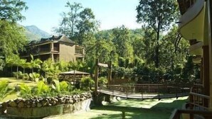 A resort with a pool surrounded by lush greenery and a stone wall. - The Rangers Reserve - Corbett (Nainital)