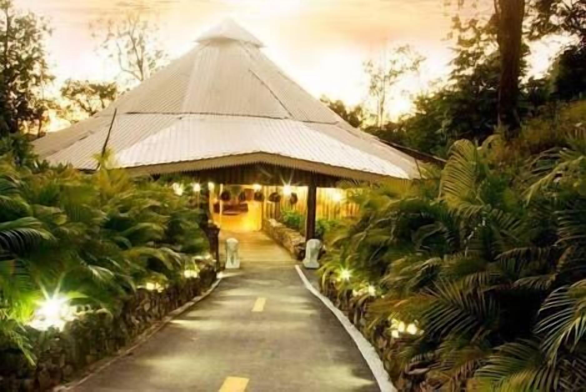 A pathway leading to a traditional-style building with a conical roof, surrounded by lush greenery.