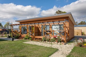 A modern wooden cabin with large windows, a deck, and a well-maintained garden.