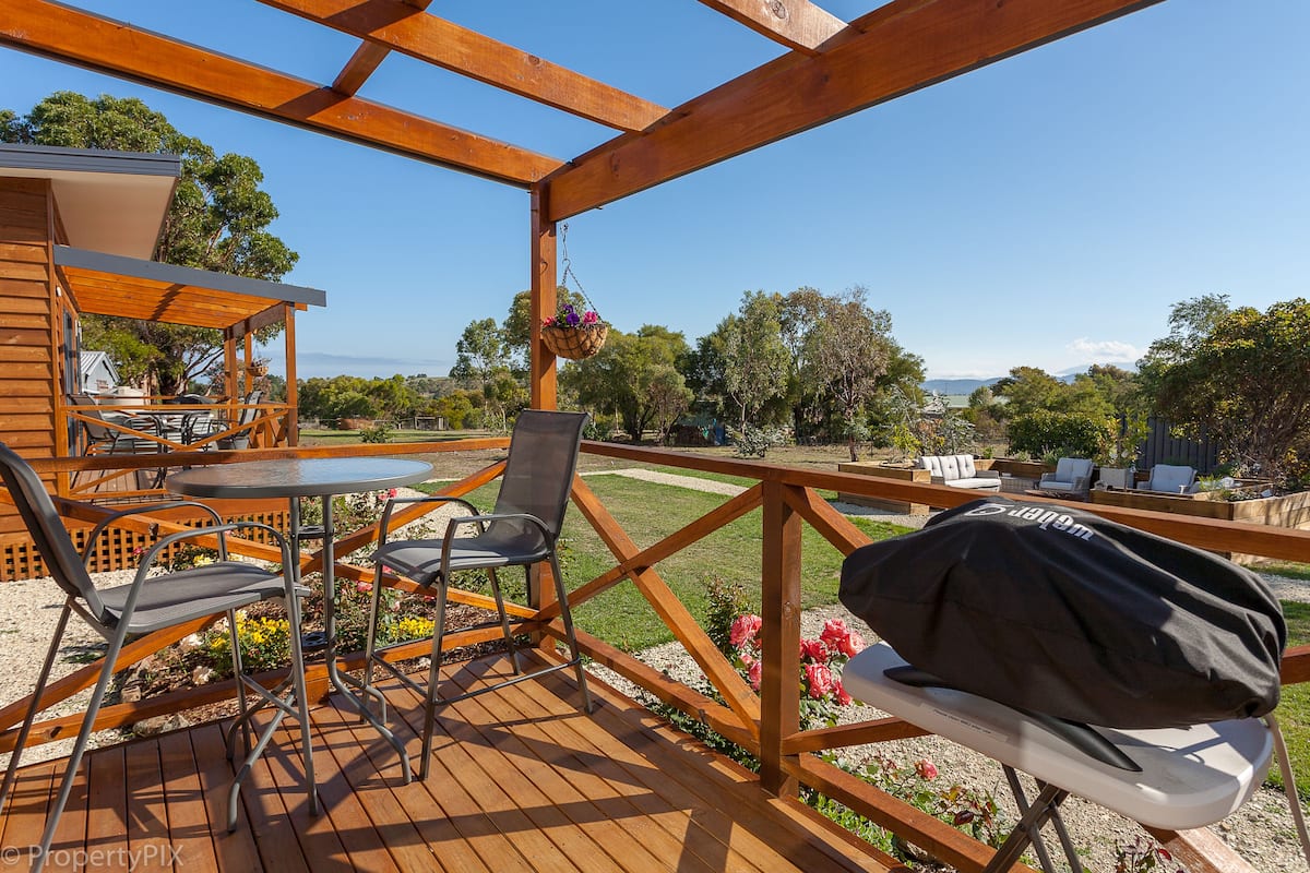 An outdoor deck with wooden furniture, a grill, and a view of the landscape.