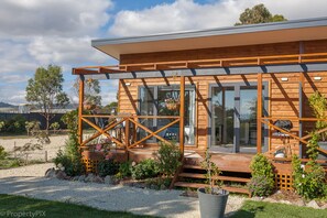 A modern wooden cabin with large windows, a covered porch, and a garden area with flowers and plants.