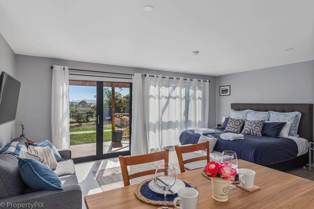 A modern bedroom with a large bed, a sofa, and a dining area with a table set for two.