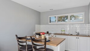 A kitchen with a wooden island, white cabinets, a window with blinds, and a tiled backsplash. - Harrison Grove (Forcett)