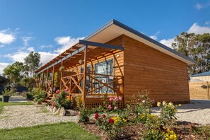 A wooden cabin with a covered patio, surrounded by a garden with various flowers and plants.