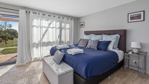 A modern bedroom with a large bed, a bench, a bedside table, and a view of the outdoors. - Harrison Grove (Forcett)