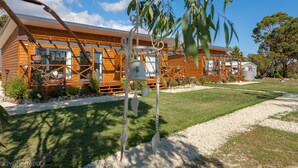 A wooden cabin with a deck, surrounded by a well-maintained lawn and gravel path. - Harrison Grove (Forcett)