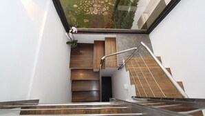 Un escalier moderne avec des marches en bois et des rampes en métal, menant à un palier où se trouve un pot de fleurs.