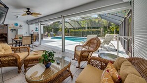 A spacious indoor patio with wicker furniture, a glass table, and a view of a swimming pool and greenery. - Villa Bonita, Located 5 Min. from Bonita Beach, WIFI, Private Lanai & Pool (Bonita Springs)