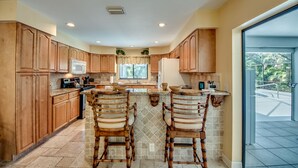 A kitchen with wooden cabinets, a central island with chairs, a microwave, and a refrigerator. - Villa Bonita, Located 5 Min. from Bonita Beach, WIFI, Private Lanai & Pool (Bonita Springs)
