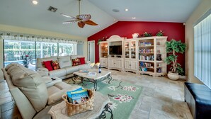 A living room with a beige sofa, a coffee table, and a bookshelf. - Villa Bonita, Located 5 Min. from Bonita Beach, WIFI, Private Lanai & Pool (Bonita Springs)