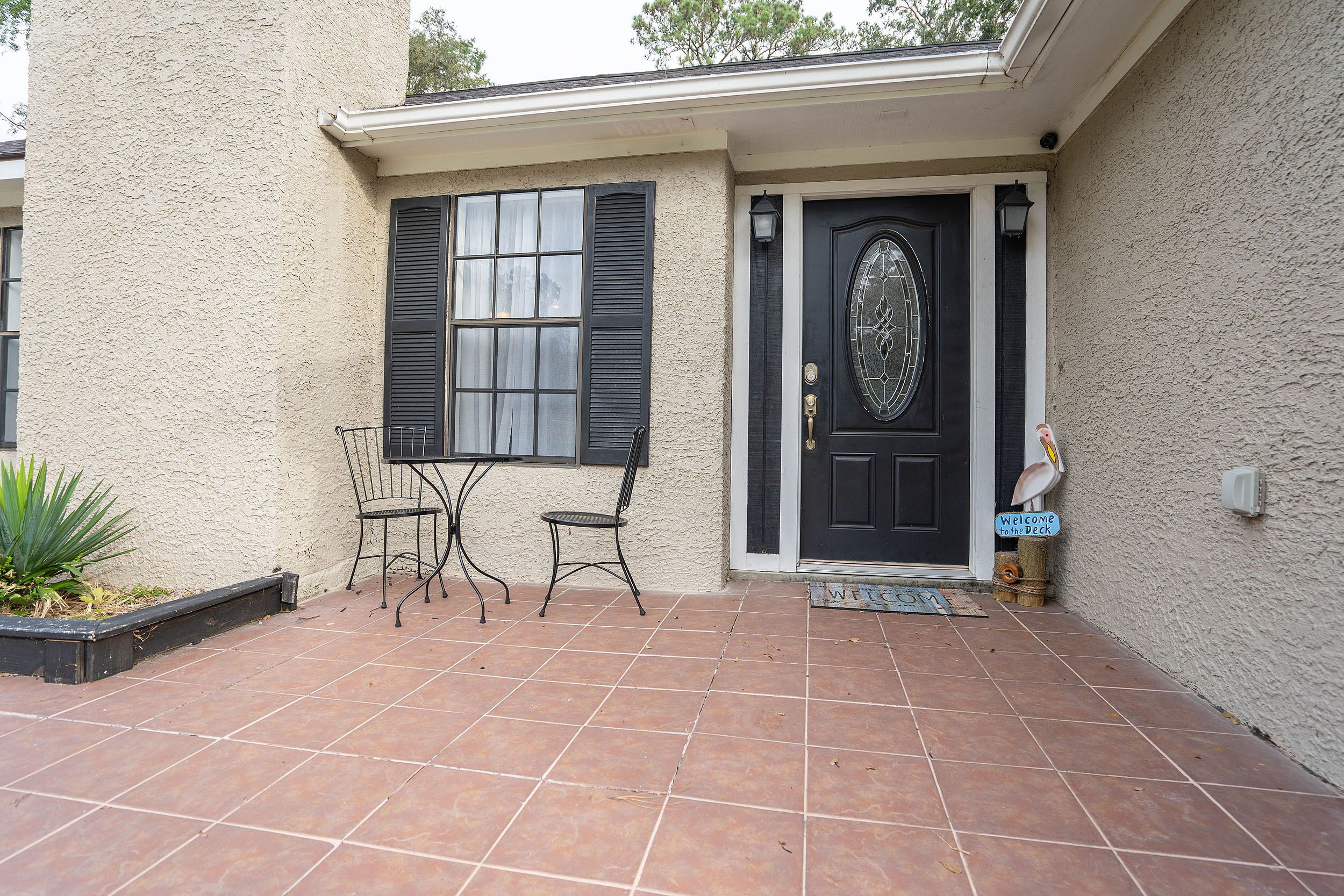 A house with a black door, a welcome sign, and a patio with two chairs and a table.