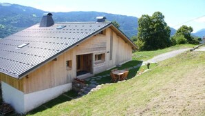 A wooden cabin with a sloped roof, a stone pathway leading to a wooden deck, and a view of mountains in the background. - Chalet - Samoens (Samoëns)