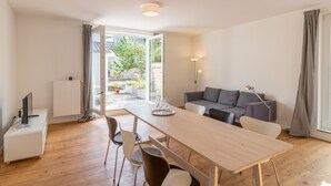 Ein modernes Wohnzimmer mit einem Holzesstisch, einer Couch und einem Fernseher auf einer Kommode.