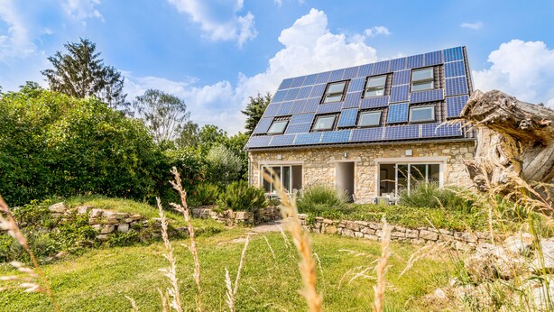 Ein modernes Haus mit Natursteinfassade, großen Fenstern und einer Solardachdeckung.