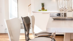 Eine moderne Küche mit weißen Schränken, einem Edelstahlbackofen und einem Essbereich mit weißem Tisch und Stühlen.
