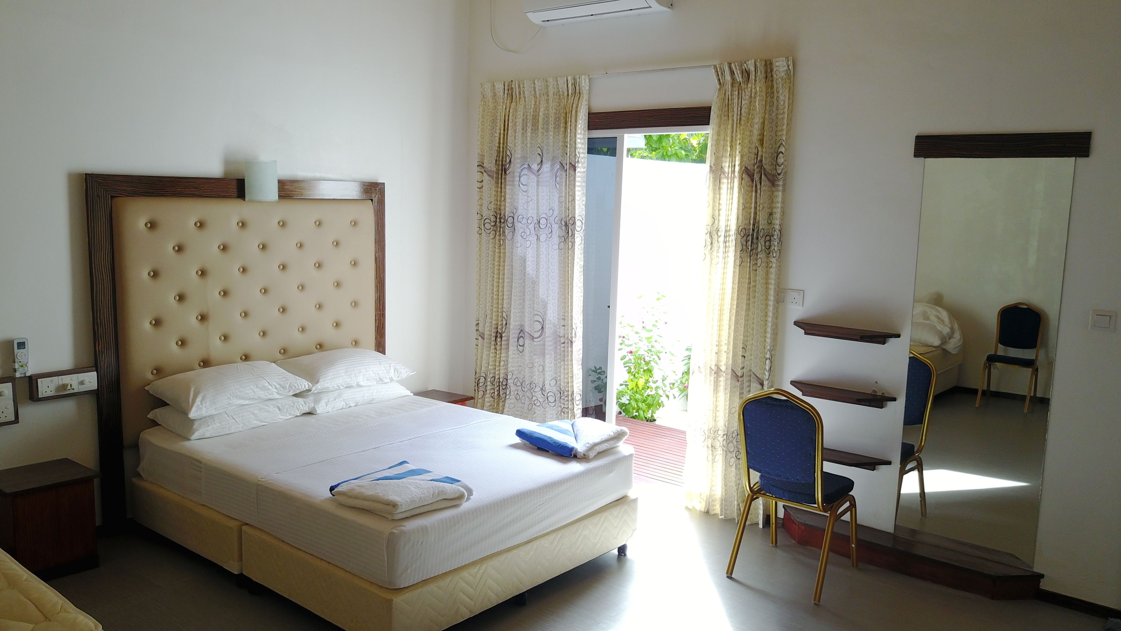 A hotel room with a large bed, a chair, a mirror, and a window with curtains.