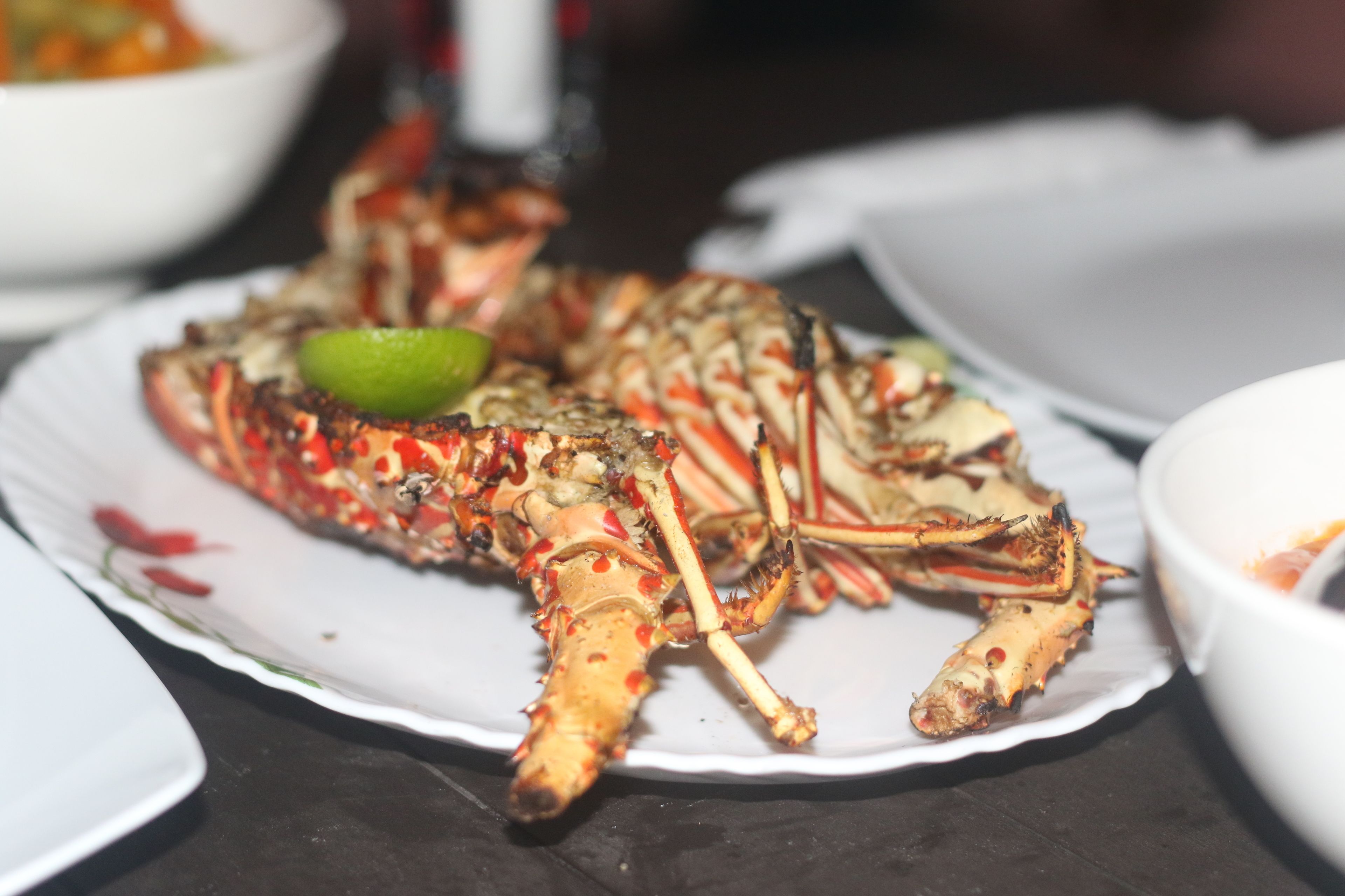 Un plato con un cangrejo cocido, una cuña de lima y un tazón blanco al fondo.