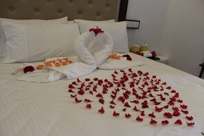 A neatly made bed with a towel arranged in a heart shape and scattered rose petals.