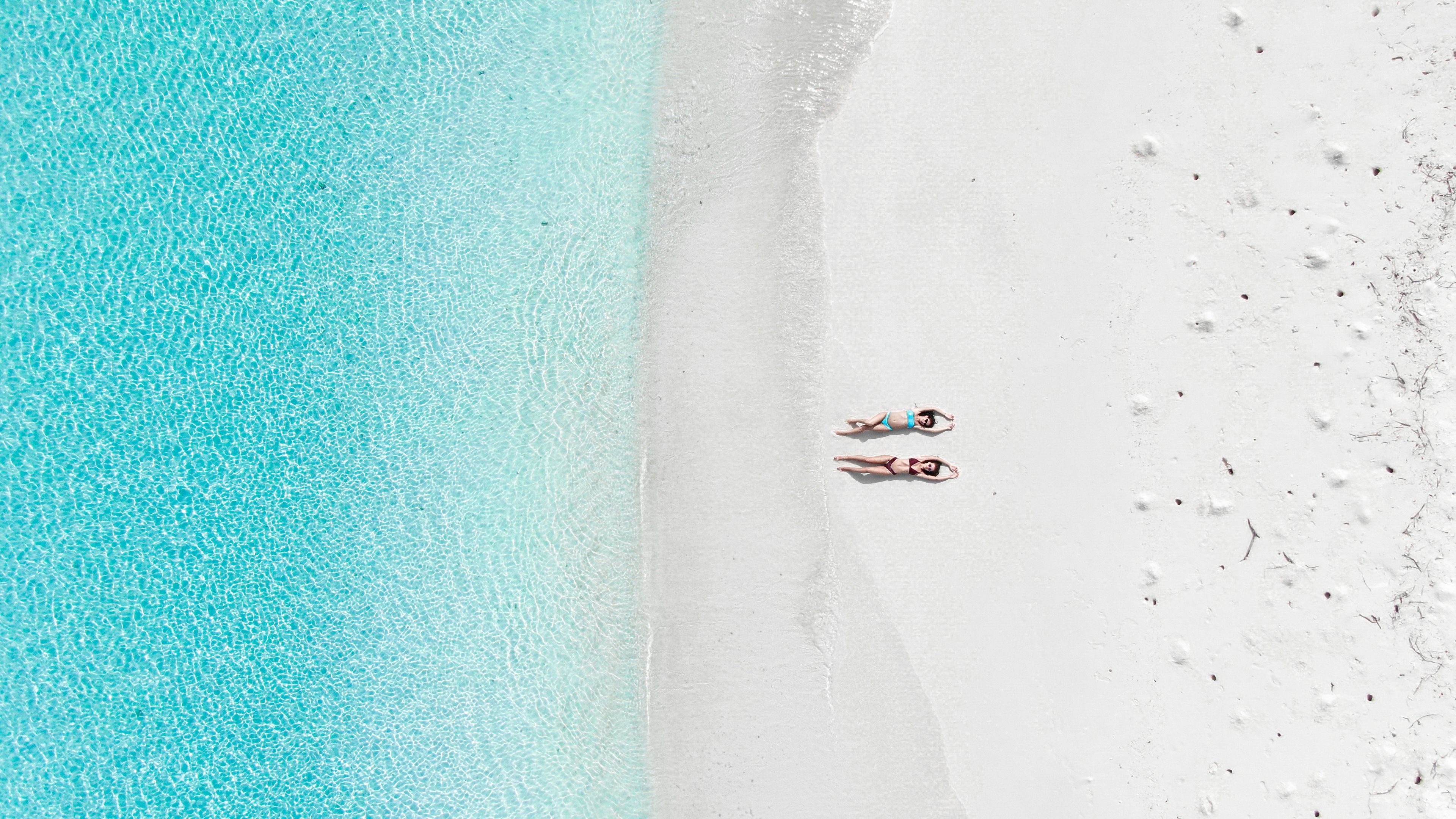 Una playa con dos personas acostadas sobre la arena, mirando al agua.